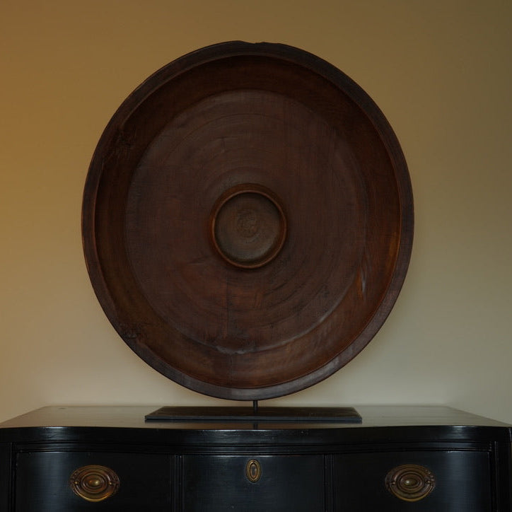 Wooden decorative plate on a black cabinet against a beige wall