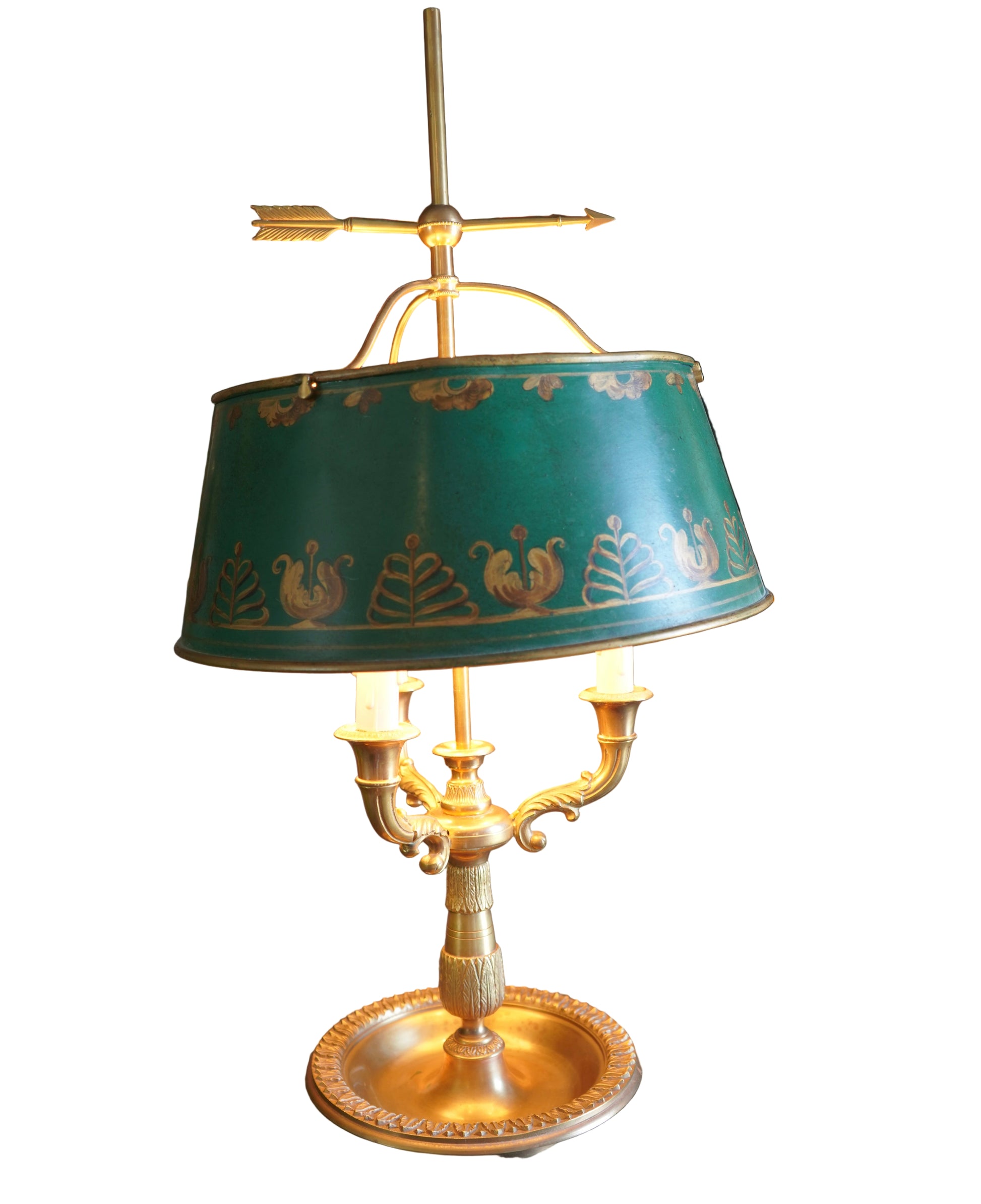 Decorative table lamp with a green shade in front of an ornate painting.