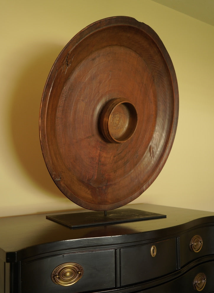 Wooden circular object on a black dresser with gold knobs against a yellow wall.