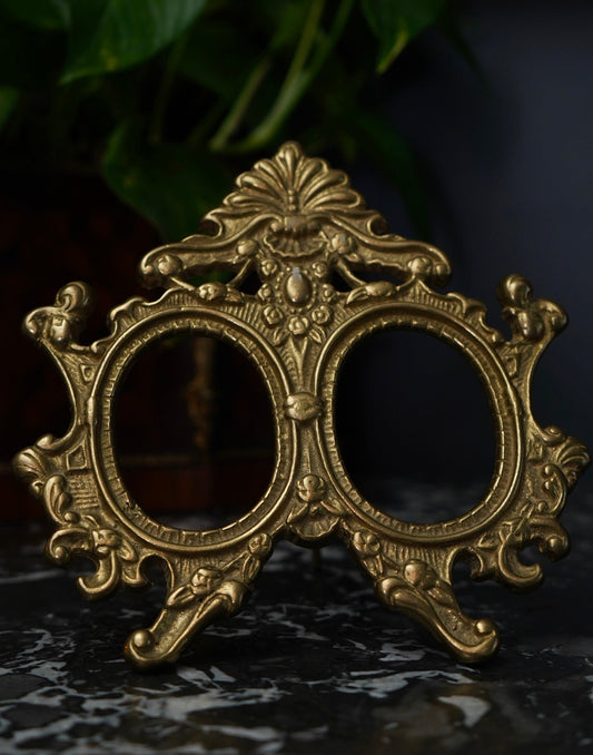 Decorative brass double oval frame on a dark surface with a blurred background
