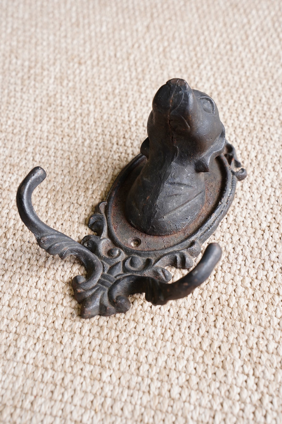An ornate black cast iron dog-shaped wall hook with decorative scrollwork, photographed on a textured beige fabric background.