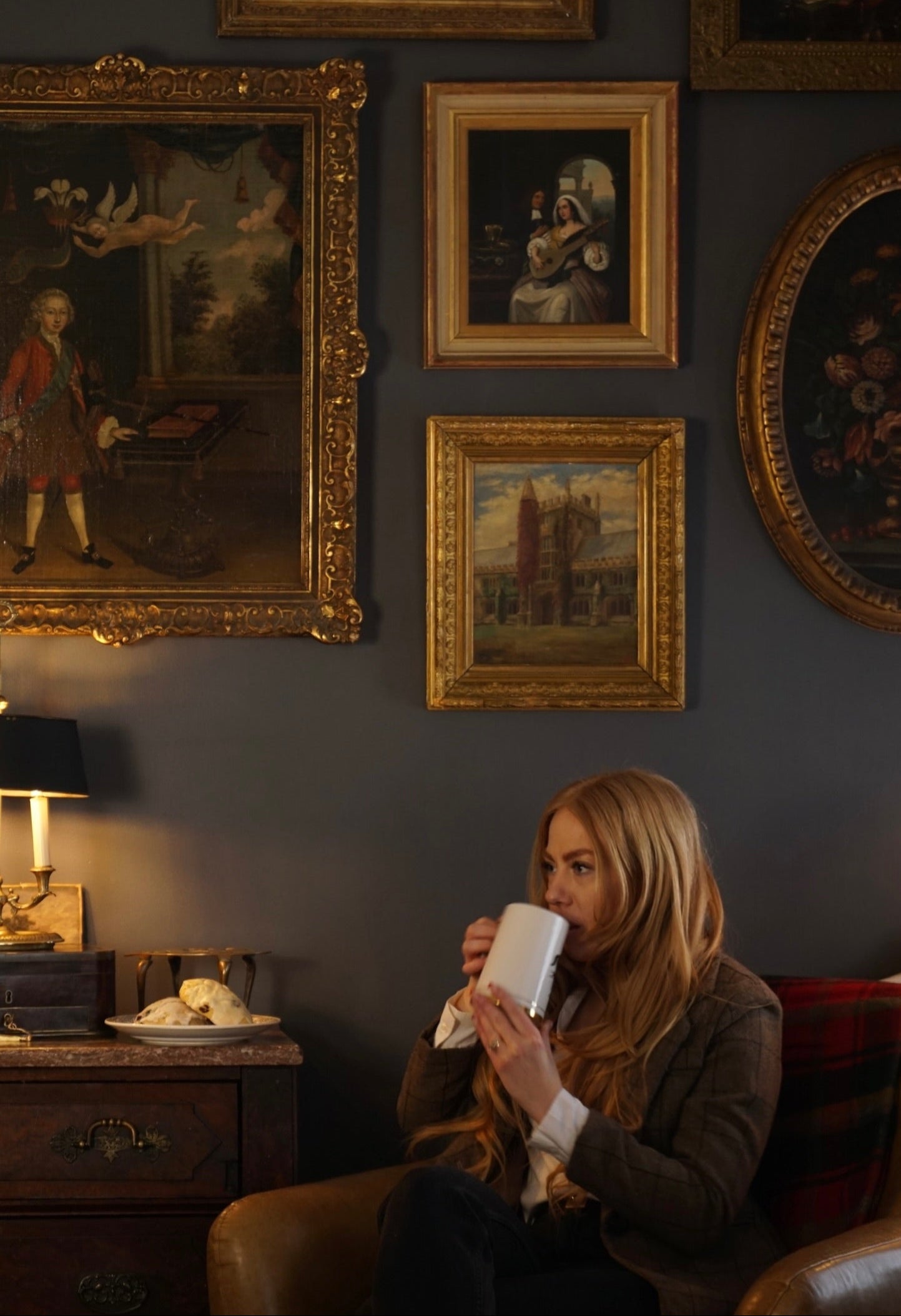 Woman sitting on a couch in a room with vintage paintings on the wall.