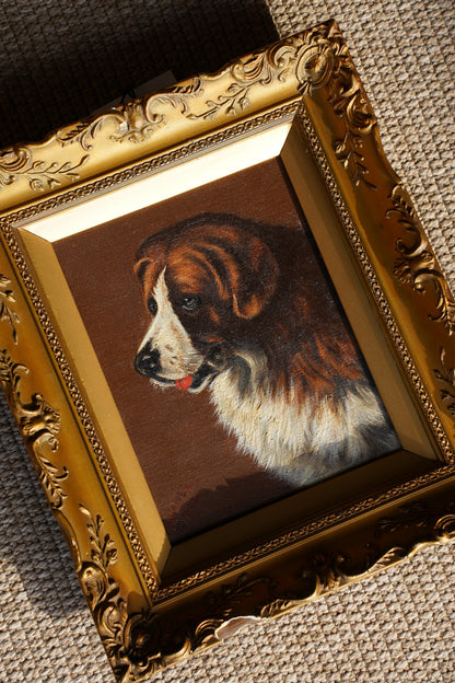 A framed custom pet portrait showing a brown and white dog looking upward, housed in an ornate gold frame, displayed on a textured beige fabric background.