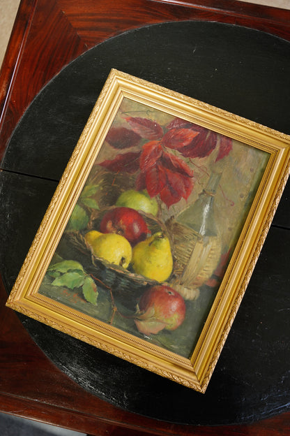 A framed still life painting of red apples, yellow pears, and green leaves, set in an ornate gold frame and displayed on a dark round table.