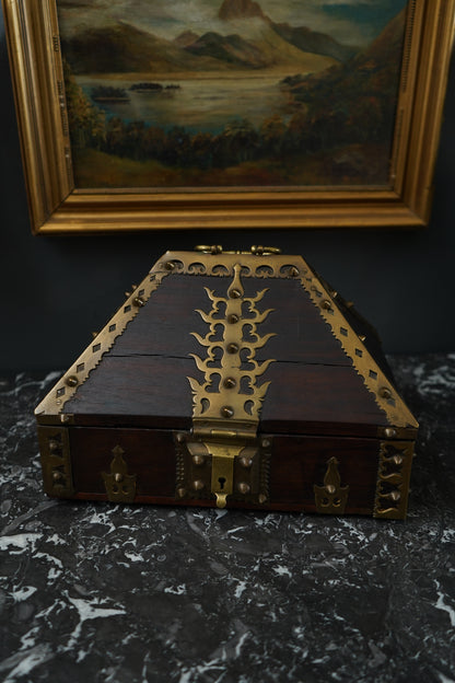 Decorative wooden box with brass hinges on a dark surface next to a framed painting.